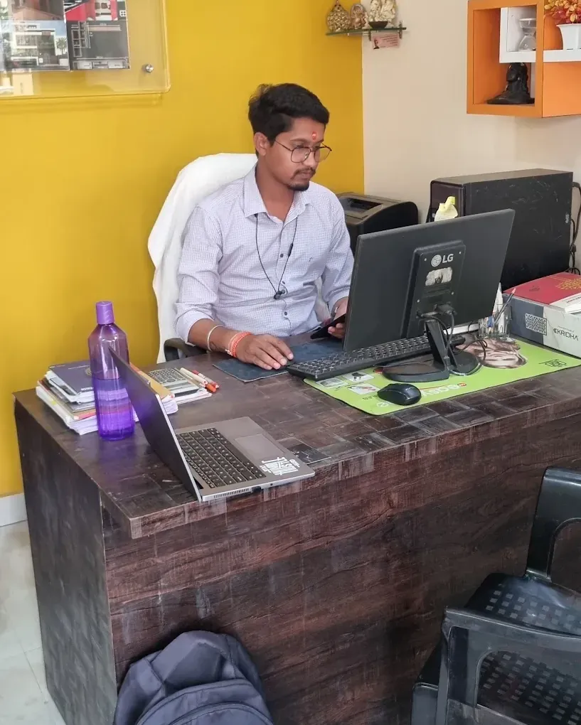 Er. Amul Damahe working at his desk in The Miraj Construction office, in front of a mustard-yellow wall
